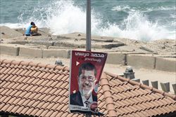 Due ragazzi egiziani si abbracciano in spiaggia, incuranti di un manifesto elettorale di Mohammed Morsy, candidato vincente dei Fratelli Musulmani (Reuters).