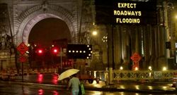 Un cartello mette in guardia i pedoni sul pericolo di inondazioni stradali davanti al Manhattan Bridge, a New York (foto AP, tratta da UsaToday.it).