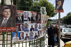 Una famiglia siriana di fronte ai manifesti elettorali a Damasco (Ansa).